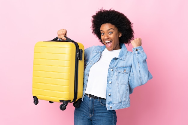 Joven mujer afroamericana en pared rosa en vacaciones con maleta de viaje
