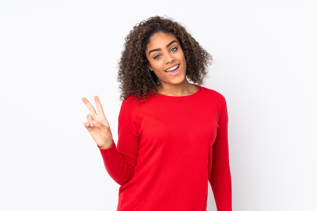 Joven mujer afroamericana en pared sonriendo y mostrando el signo de la victoria