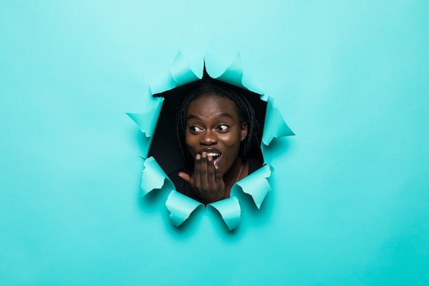 Joven mujer afroamericana posando desde el agujero de papel amarillo