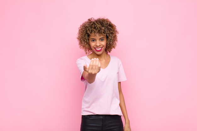 Joven mujer afroamericana que se siente feliz, exitosa y segura, enfrenta un desafío y dice ¡adelante! o darte la bienvenida en la pared rosa