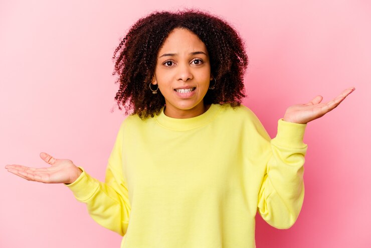 Foto joven mujer afroamericana de raza mixta aislada confundida y dudosa encogiéndose de hombros para mantener un espacio de copia.