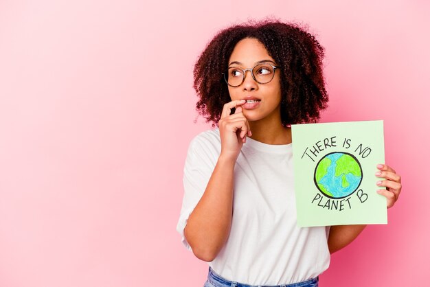 Joven mujer afroamericana de raza mixta sosteniendo un cartón de concepto de protección mundial relajado pensando en algo mirando un espacio de copia.