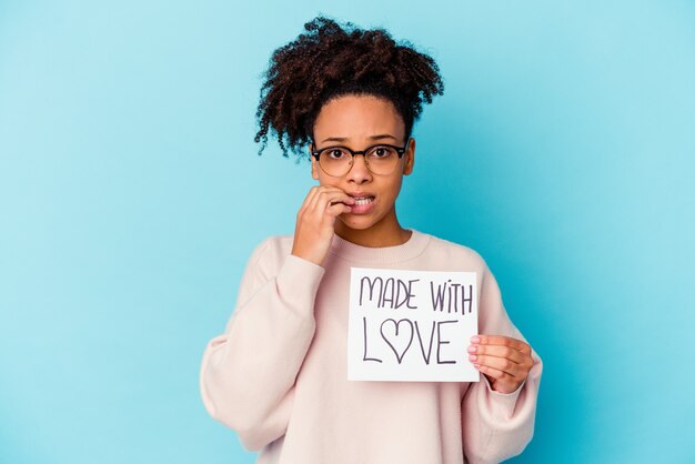 Joven mujer afroamericana de raza mixta sosteniendo un concepto hecho con amor mordiéndose las uñas, nervioso y muy ansioso.