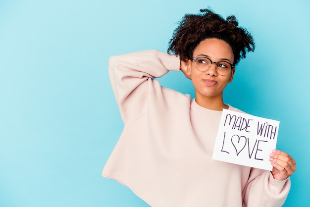 Joven mujer afroamericana de raza mixta sosteniendo un concepto hecho con amor tocando la parte posterior de la cabeza, pensando y tomando una decisión.