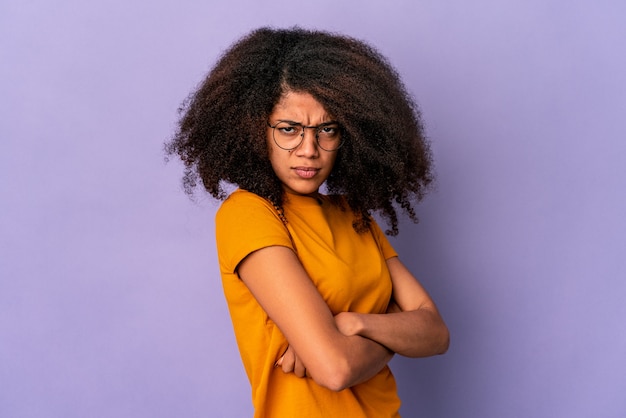 Joven mujer afroamericana rizada aislada en la pared púrpura con el ceño fruncido en disgusto, mantiene los brazos cruzados.