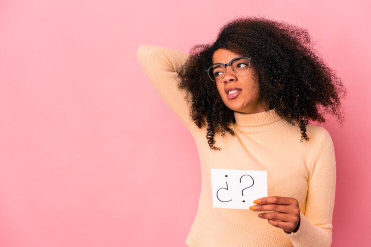 Foto joven mujer afroamericana rizada sosteniendo un interrogatorio en un cartel tocando la parte posterior de la cabeza, pensando y tomando una decisión.