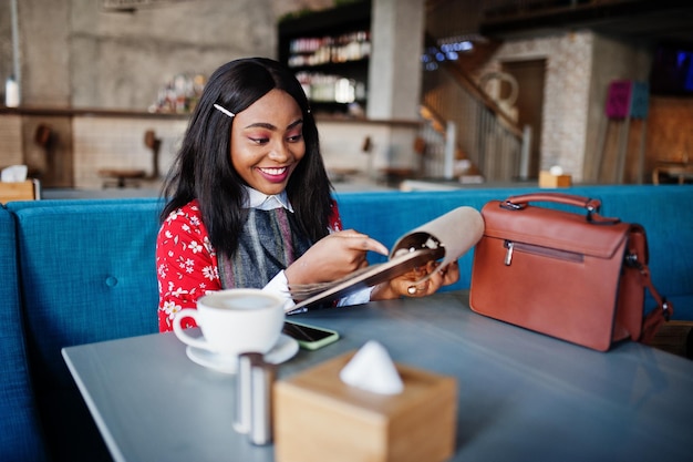 Joven mujer afroamericana segura de sí misma con ropa informal elegante en el menú de lectura del café