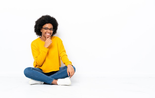 Joven mujer afroamericana sentada en el suelo con gafas y sonriendo