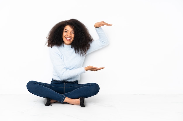 Joven mujer afroamericana sentada en el suelo sosteniendo copyspace para insertar un anuncio