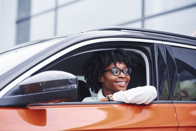 Joven mujer afroamericana se sienta dentro del coche nuevo y moderno.