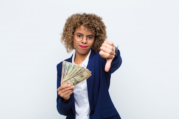 Joven mujer afroamericana se siente cruzada, enojada, molesta, decepcionada o disgustada, mostrando los pulgares hacia abajo con una mirada seria con billetes en euros