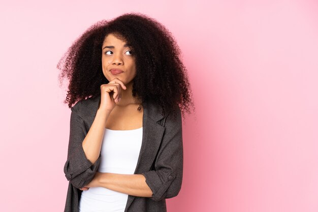 Joven mujer afroamericana sobre pared aislada teniendo dudas y pensamiento