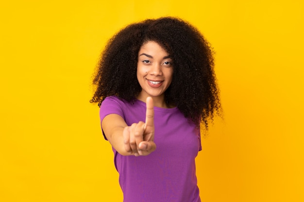 Joven mujer afroamericana sobre pared mostrando y levantando un dedo