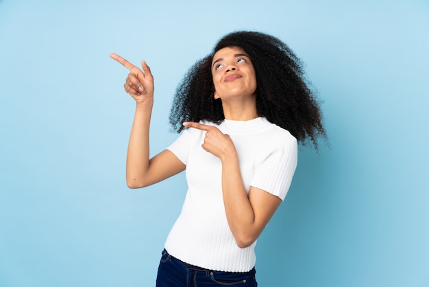 Joven mujer afroamericana sobre la pared señalando con el dedo índice una gran idea