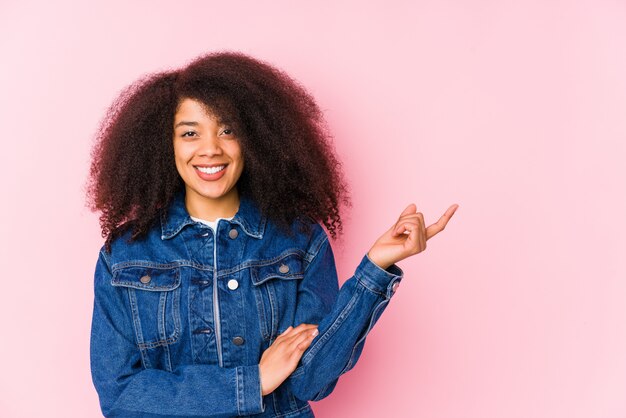 Joven mujer afroamericana sonriendo alegremente señalando con el dedo lejos.