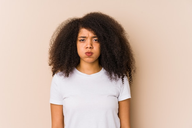 Joven mujer afroamericana sopla mejillas, tiene expresión cansada. Concepto de expresión facial