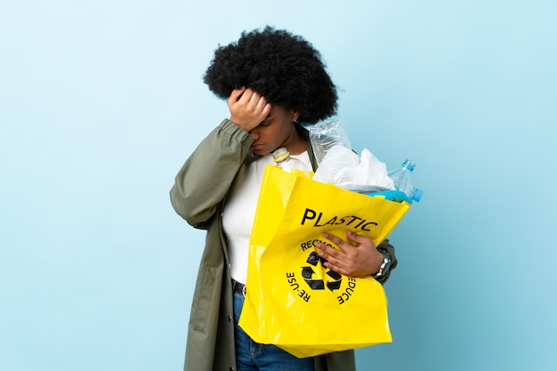 Joven mujer afroamericana sosteniendo una bolsa de reciclaje en la pared colorida con dolor de cabeza