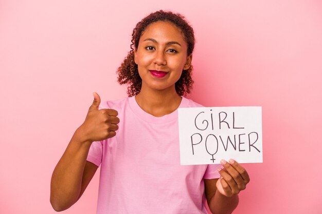 Joven mujer afroamericana sosteniendo un cartel de poder femenino aislado sobre fondo de color rosa