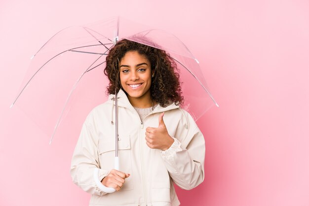 Joven mujer afroamericana sosteniendo un paraguas sonriendo y levantando el pulgar