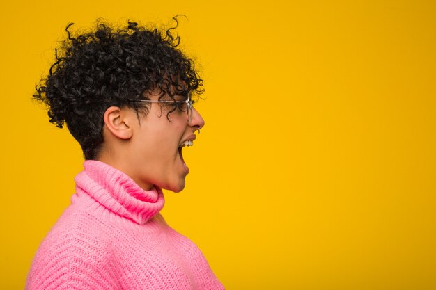 Joven mujer afroamericana vistiendo un suéter rosa gritando hacia un espacio de copia