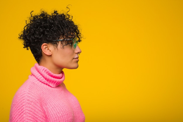 Joven mujer afroamericana vistiendo un suéter rosa mirando hacia la izquierda, de lado plantean.