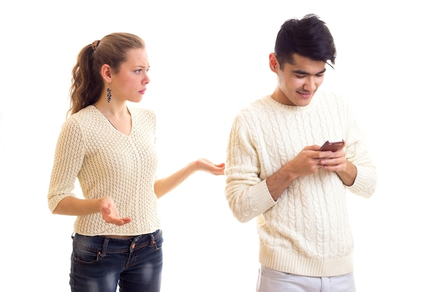 Joven mujer agradable con un joven inteligente con suéteres blancos y jeans usando un teléfono inteligente