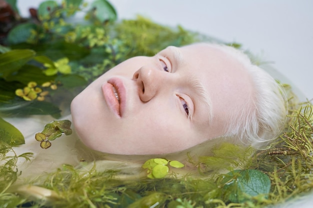 Joven mujer albina con piel pálida tomando un baño relajante con hierbas