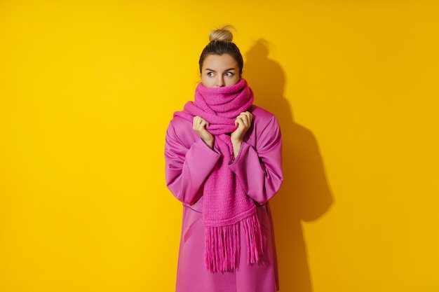 Joven mujer alegre con abrigo rosa y bufanda de lana con fondo amarillo