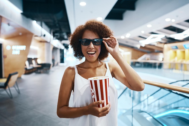 Joven mujer alegre con gafas 3d con palomitas de maíz en las manos yendo al cine