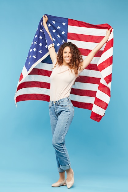 Joven mujer alegre con pelo largo y rizado oscuro con bandera de Estados Unidos