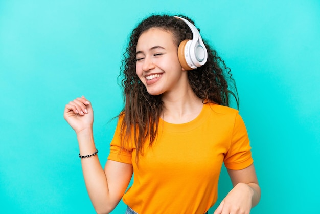 Joven mujer árabe aislada de fondo azul escuchando música y bailando