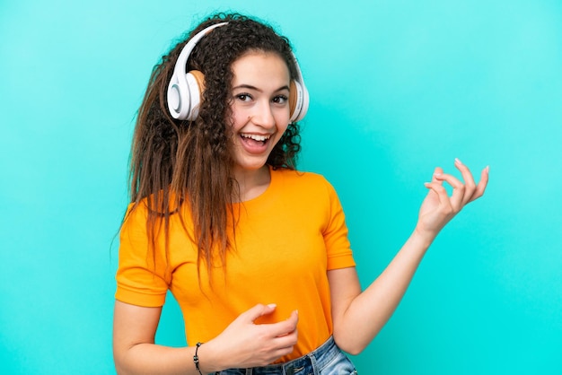 Joven mujer árabe aislada de fondo azul escuchando música y haciendo gestos de guitarra