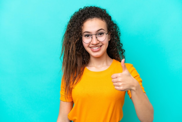 Joven mujer árabe aislada de fondo azul con gafas y con el pulgar hacia arriba