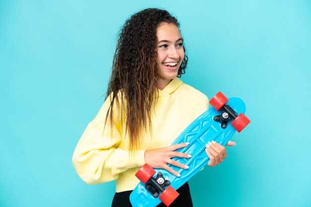 Joven mujer árabe aislada de fondo azul con un patín con expresión feliz