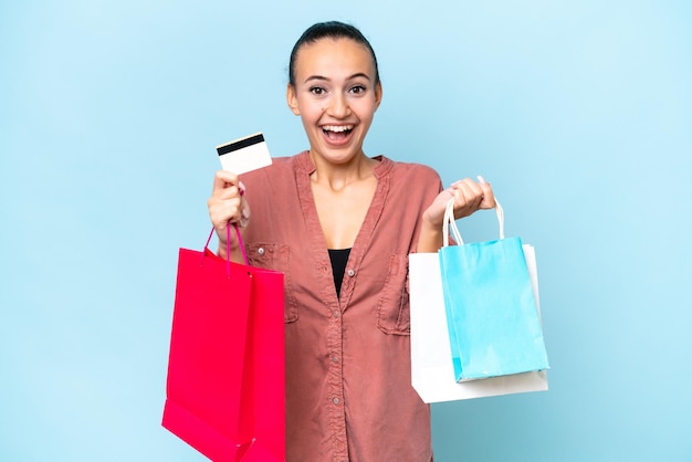 Joven mujer árabe aislada de fondo azul sosteniendo bolsas de compras y sorprendida