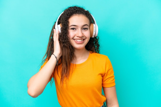 Joven mujer árabe aislada sobre fondo azul escuchando música