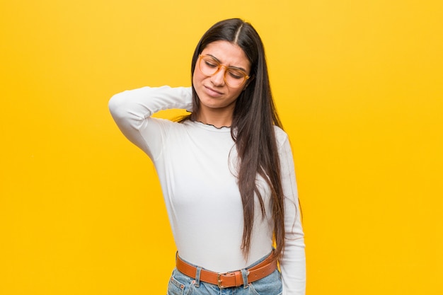 Foto joven mujer árabe bonita contra una pared amarilla que sufre dolor de cuello debido al estilo de vida sedentario.