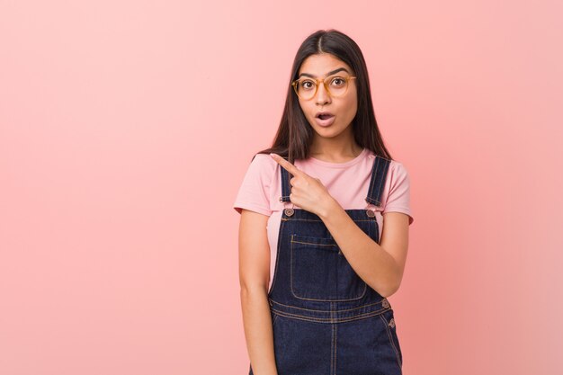 Joven mujer árabe bonita vistiendo un mono de jeans apuntando hacia el lado