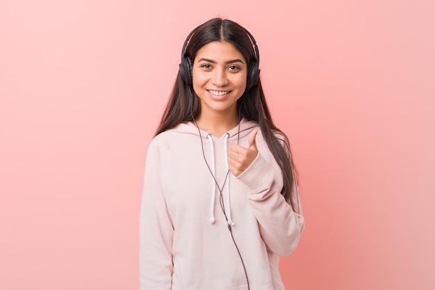 Joven mujer árabe escuchando música sonriendo y levantando el pulgar hacia arriba