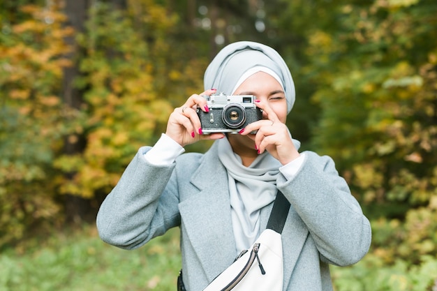 Joven mujer árabe con pañuelo hijab fotografiando con un teléfono inteligente en el parque. Chica musulmana moderna