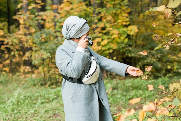Joven mujer árabe con pañuelo hijab fotografiando con un teléfono inteligente en el parque. Chica musulmana moderna