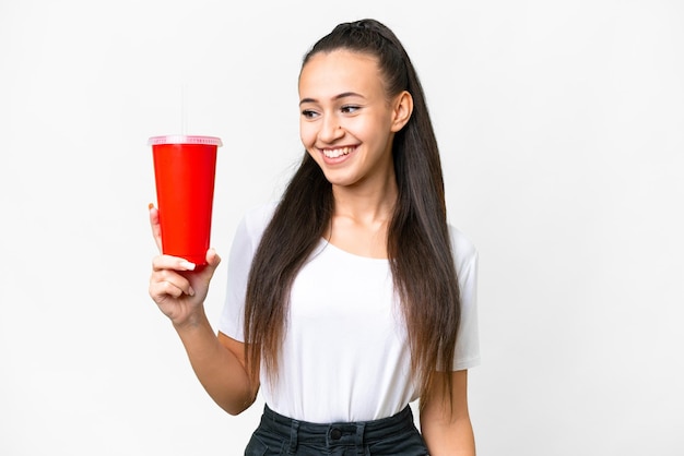 Joven mujer árabe sosteniendo soda sobre fondo blanco aislado con expresión feliz