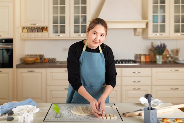 Joven mujer de Asia central está cocinando en el interior de una cocina casera moderna