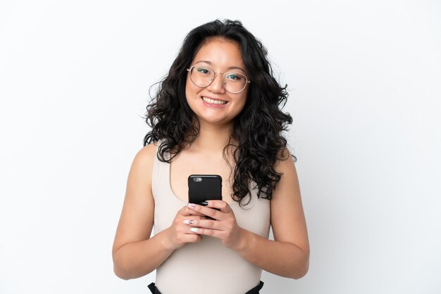 Joven mujer asiática aislada sobre fondo blanco mirando a la cámara y sonriendo mientras usa el móvil