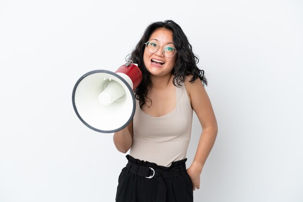 Joven mujer asiática aislada sobre fondo blanco sosteniendo un megáfono y con expresión de sorpresa