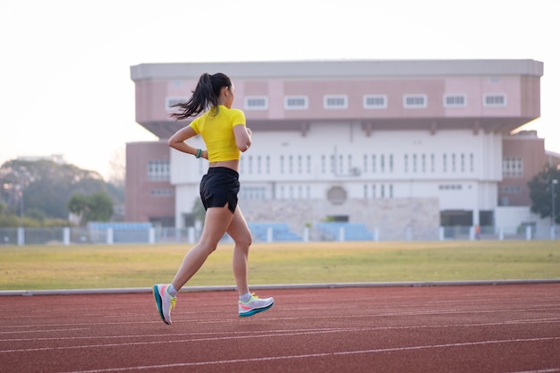 Una joven mujer asiática atleta corredor trotar en la pista de atletismo en el estadio de la ciudad en la mañana soleada para mantener la aptitud y el estilo de vida saludable. Mujer joven fitness se ejecuta en la pista del estadio. Deporte y recreación