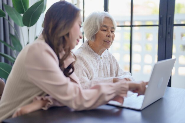 Joven mujer asiática ayudando a su abuela por usar su nueva computadora portátil