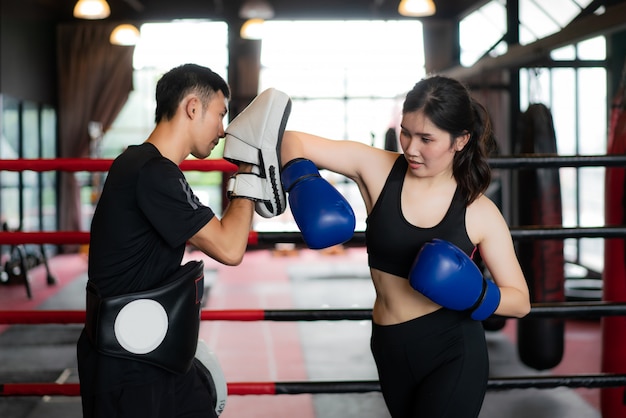 Joven mujer asiática boxeador golpea con un codo al entrenador profesional en el estadio de boxeo