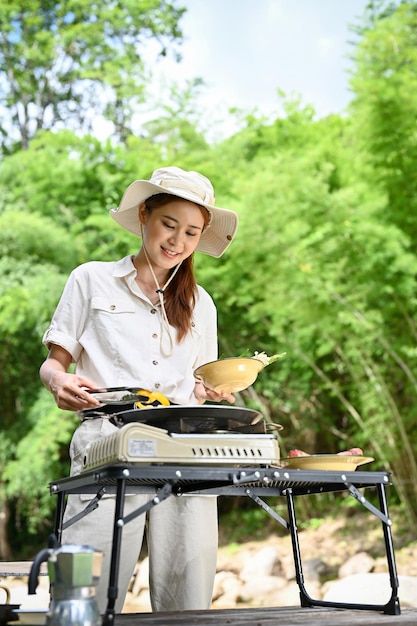Joven mujer asiática en el campamento preparando comida de fiesta de picnic barbacoa asando un bistec