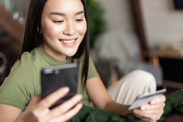 Joven mujer asiática comprando en una tienda en línea mediante teléfono móvil y compras con tarjeta de crédito desde casa